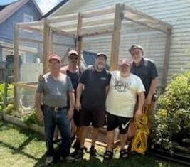 A group of six men from Wabash's Hesed men's community standing together in front of the chicken coop they finished building